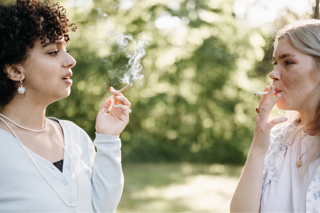 Two women smoking cigarettes outdoors on a trail
